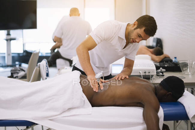 Фізіотерапевт лікує чоловіка, використовуючи обладнання для радіотерапії — стокове фото