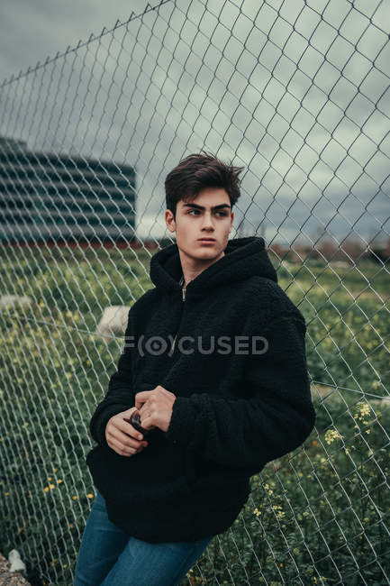 Junger schöner Mann mit Plastikflasche am Zaun im Nebel — Stockfoto