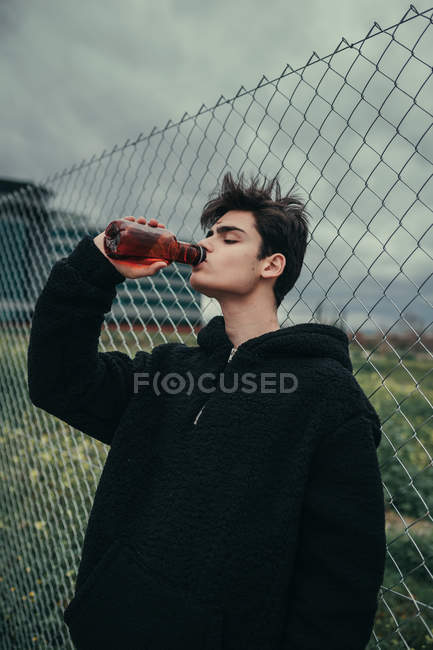 Giovane bell'uomo che beve dalla bottiglia di plastica alla recinzione — Foto stock