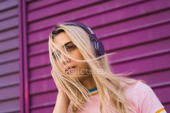 Mujer joven con auriculares morados de pie contra la pared morada - foto de stock