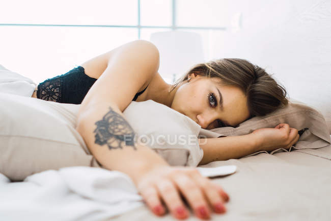 Заманчивая женщина с татуировкой в черном лежит на кровати — стоковое фото