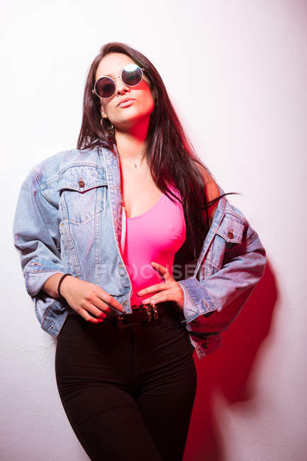 Giovane donna vestita di rosa con gli occhiali da sole in piedi al muro bianco e guardando la fotocamera — Foto stock