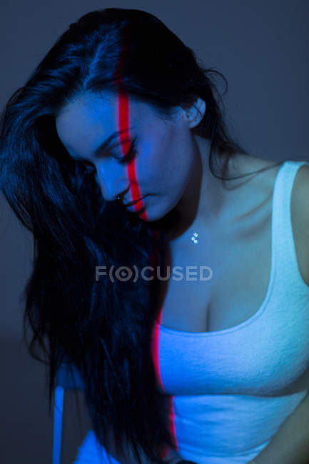 Mujer atractiva joven con línea roja en la cara y el cuerpo mirando hacia abajo sobre fondo oscuro - foto de stock