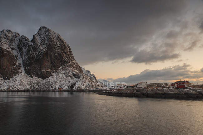Agua de mar oscura y montañas rocosas bajo el cielo nublado, Hamnoy, Noruega - foto de stock