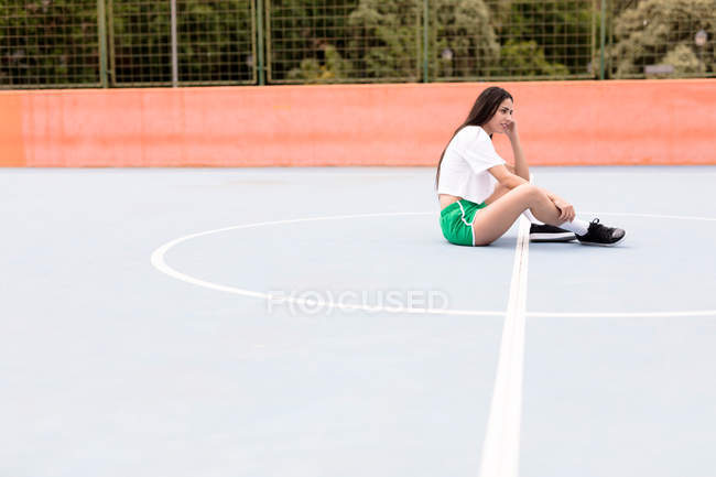Jeune femme assise sur un terrain de sport — Photo de stock