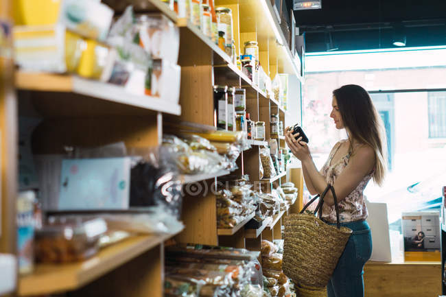Young woman picking up jam jar in store — Stock Photo