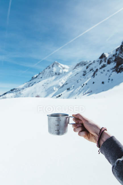 Main de touriste méconnaissable tenant tasse en métal dans les montagnes en hiver — Photo de stock