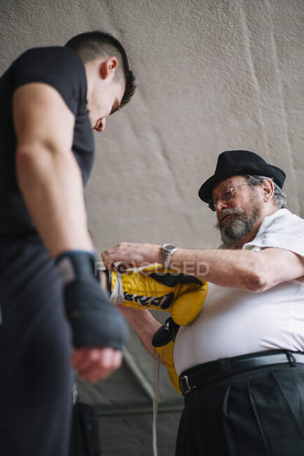 Entrenador adulto atando guante de boxeador en la mano del deportista en el ring. - foto de stock