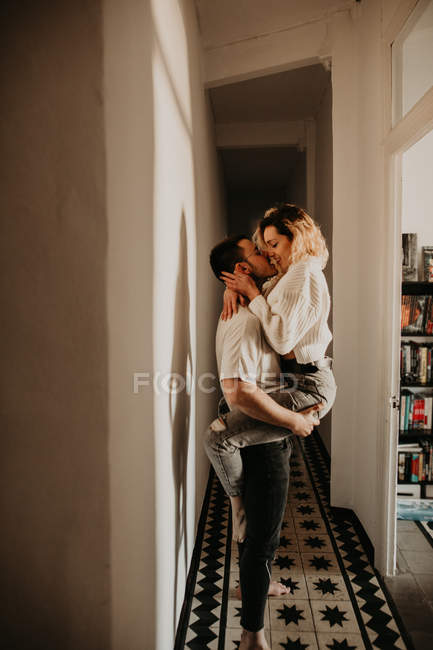 Страстный мужчина и женщина обнимаются и целуются у стены в холле дома — стоковое фото