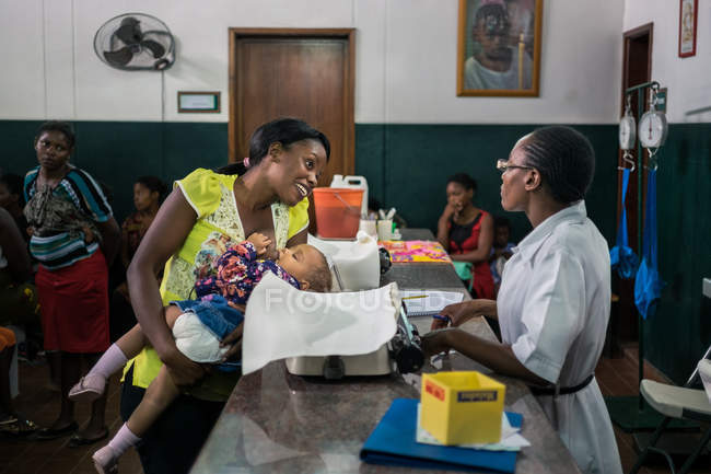 ANGOLA - ÁFRICA - 5 DE ABRIL DE 2018 - sonriente mujer negra interactuando con la enfermera en la recepción en el hospital - foto de stock