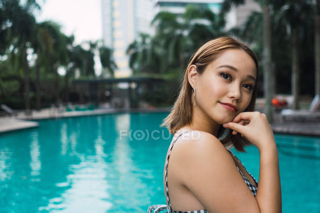 Retrato de mulher sorridente em pé à beira da piscina — Fotografia de Stock