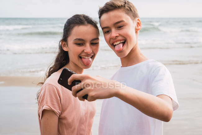 Dos adolescentes sonrientes tomando selfie en la orilla del mar - foto de stock