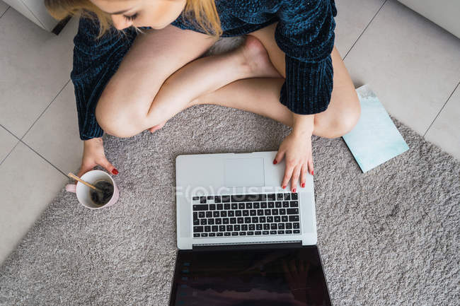 Femme avec ordinateur portable et café assis sur le sol à la maison — Photo de stock