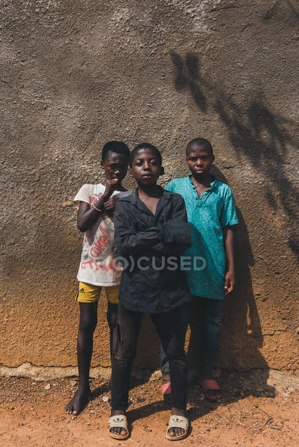 CAMARÕES - ÁFRICA - 5 DE ABRIL DE 2018: Meninos africanos alegres e duros em pé na parede áspera e olhando para a câmera — Fotografia de Stock