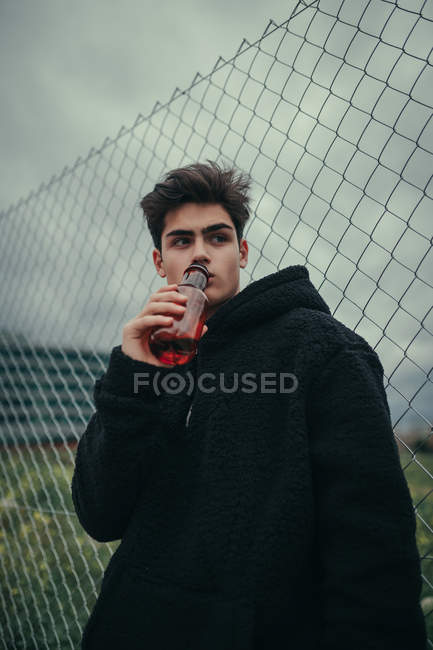 Young handsome man drinking from plastic bottle at fence — Stock Photo