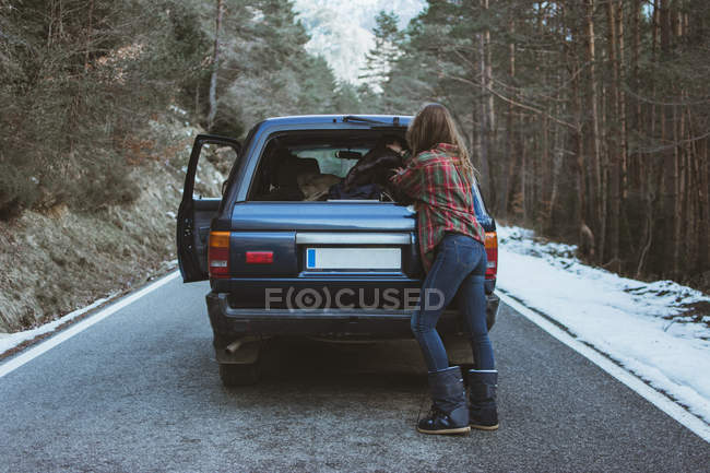 Woman packing stuff to trunk of car on road in winter forest — Stock Photo