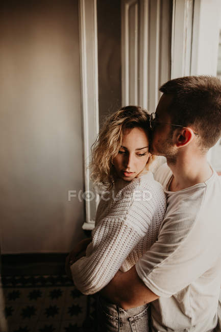 Romantica giovane coppia che abbraccia alla finestra a casa — Foto stock
