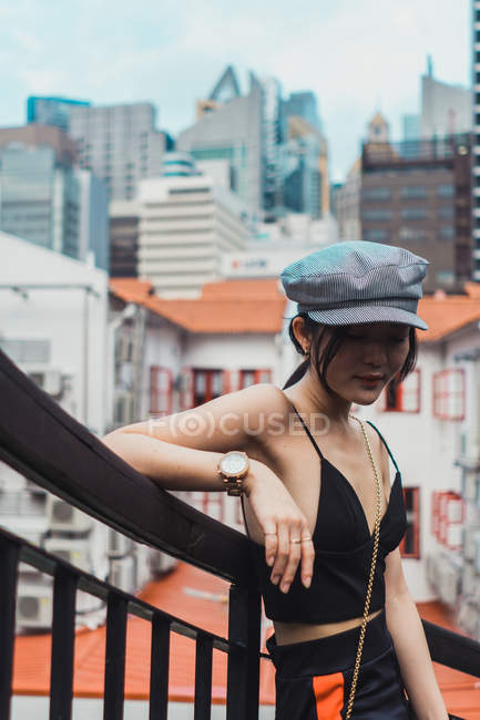 Jovem mulher asiática em roupas elegantes inclinando-se sobre cerca na cidade — Fotografia de Stock