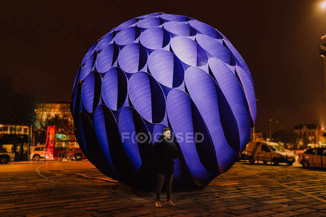 Uomo in piedi davanti a un grande monumento a sfera blu illuminato di notte, Oporto, Portogallo — Foto stock