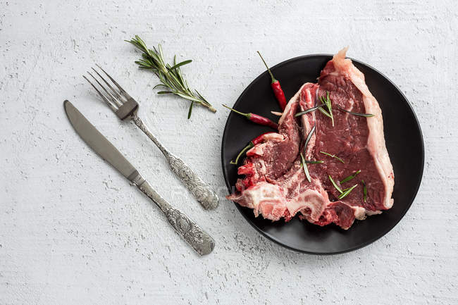 Steak de boeuf cru sur assiette noire avec couteau et fourchette — Photo de stock