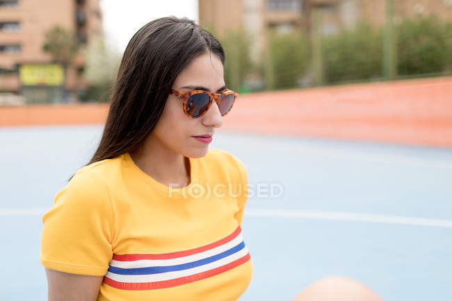 Jeune femme en lunettes de soleil assis sur le terrain de sport — Photo de stock
