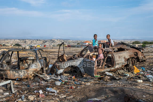 ANGOLA - ÁFRICA - 5 de abril de 2018 - Niños africanos de pie y jugando en un coche gruñón en el vertedero - foto de stock