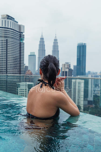 Азіатський жінка розслабляючий в басейн з видом на місто на тлі — стокове фото