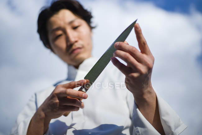 Japanischer Koch checkt Messer vor blauem Himmel — Stockfoto