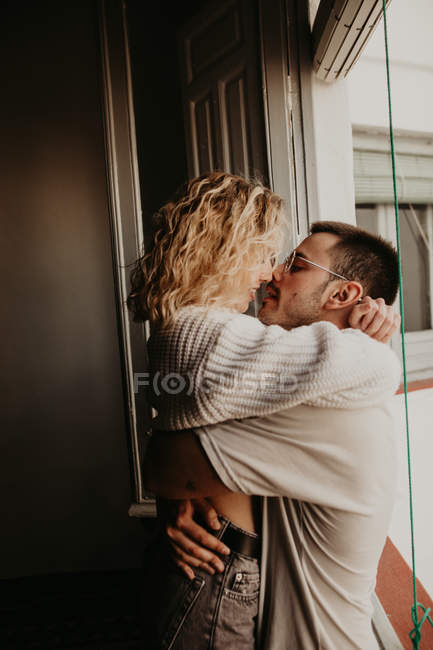 Cariñosa pareja abrazando en ventana en casa - foto de stock