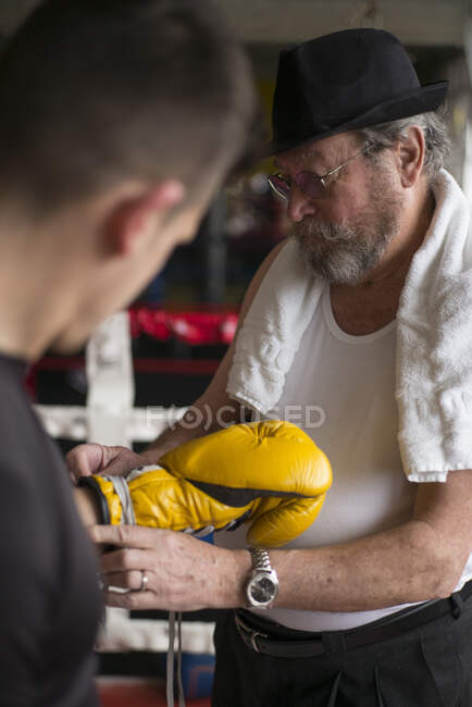 Entraîneur adulte attachant gant de boxer sur la main du sportif dans l'anneau. — Photo de stock