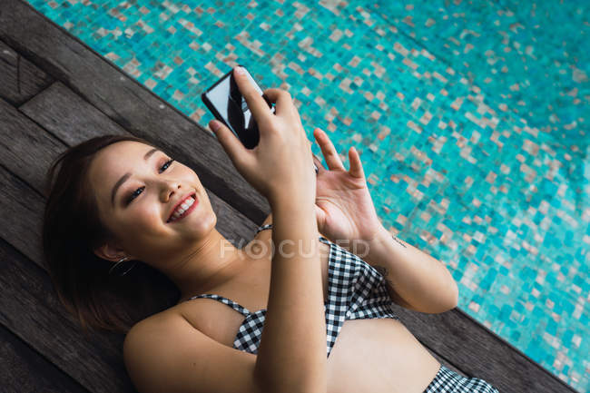 Lächelnde Frau mit Smartphone entspannt am Pool — Stockfoto