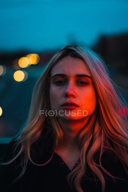 Nachdenkliche blonde Frau blickt in der Abenddämmerung in die Kamera — Stockfoto