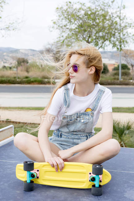 Menina loira sentada no chão com penny board — Fotografia de Stock