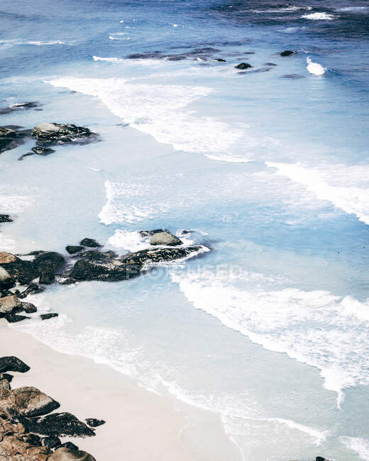 Desde arriba la costa arenosa con las rocas y el océano azul en el día soleado. - foto de stock