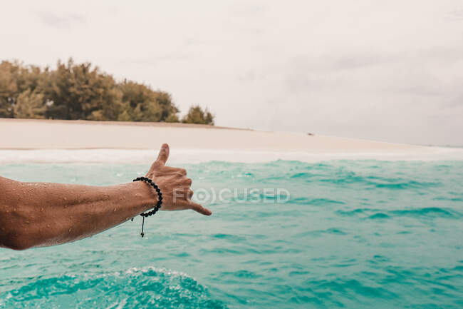 Crop hand of person in turquoise ocean gesturing shaka at the coast. — Stock Photo
