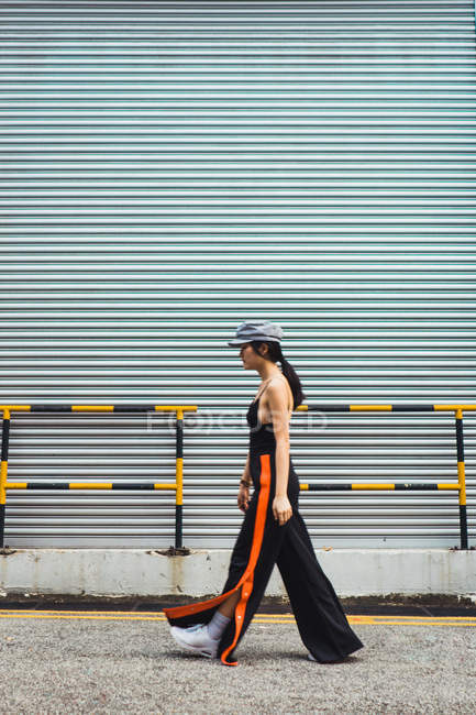 Elegante mujer asiática joven caminando delante de la pared de metal - foto de stock