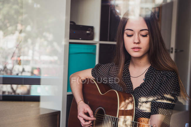 Jeune femme jouant de la guitare à la fenêtre — Photo de stock