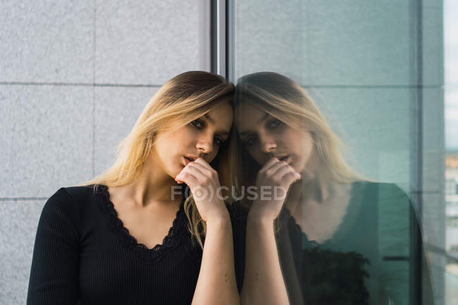 Porträt einer selbstbewussten Frau in Schwarz, die sich an eine Glaswand lehnt — Stockfoto
