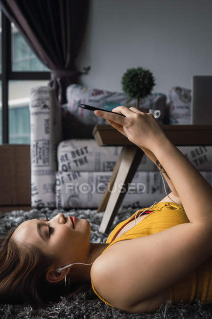 Femme asiatique couché et relaxant avec smartphone sur le sol à la maison — Photo de stock
