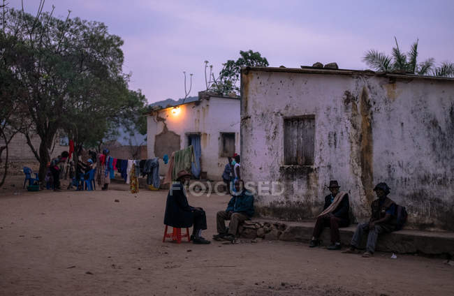 ANGOLA - ÁFRICA - 5 DE ABRIL DE 2018 - Etnia de pé e sentada na rua da aldeia em casas grunhidas à noite — Fotografia de Stock