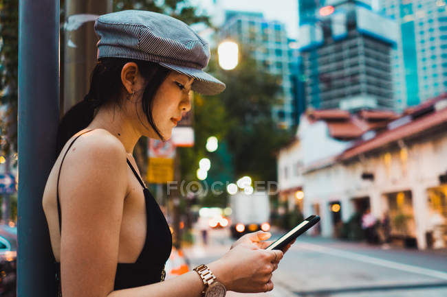 Mulher asiática em roupas elegantes usando smartphone na rua na cidade — Fotografia de Stock
