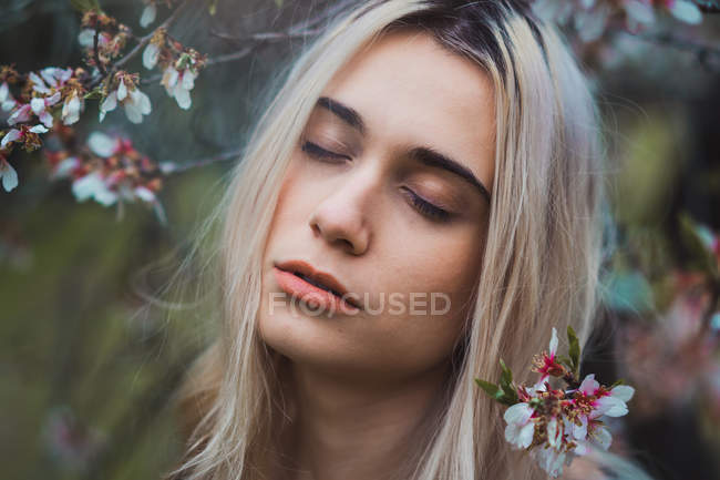 Portrait of young blonde woman in flowers with closed eyes — Stock Photo