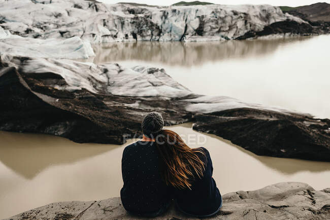 Back view of unrecognizable couple sitting and looking at dirty small lakes in hillside. — Stock Photo