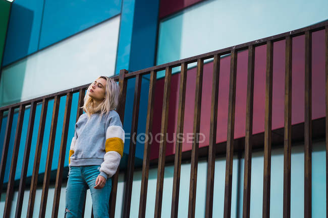 Pretty blonde woman standing at fence against on colorful modern houses — Stock Photo