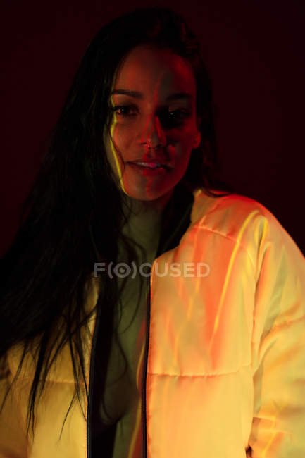 Pretty young woman in white jacket with light stains on face looking at camera on dark background — Stock Photo
