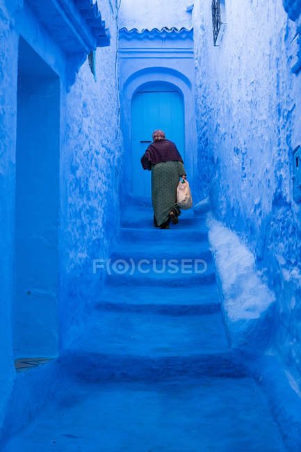 Anciana subiendo las escaleras azules en Marruecos - foto de stock
