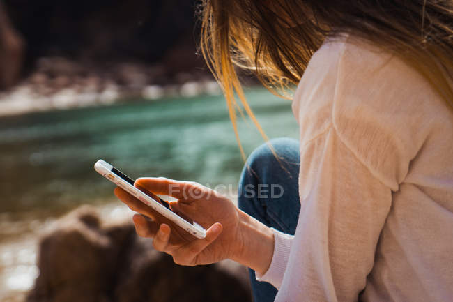 Mujer usando smartphone en rocas a orillas del mar - foto de stock