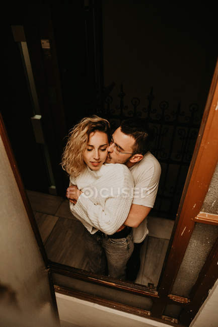 Cheerful man and woman standing and embracing at window at home — Stock Photo