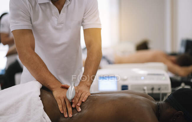 Le physiothérapeute traitant un homme utilisant un équipement pour la radiothérapie — Photo de stock