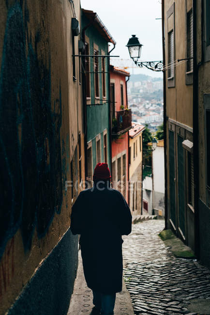 Vista traseira do homem de chapéu vermelho descendo a rua estreita na cidade velha, Porto, Portugal — Fotografia de Stock